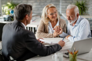 Happy senior woman encourages her husband to sign a contract with their bank manager during a meeting in the office